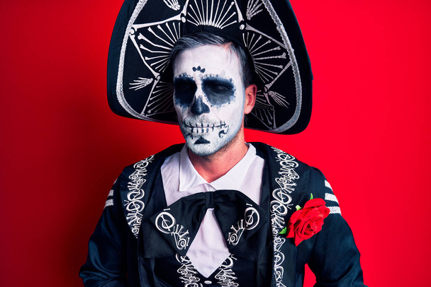 Молодой человек, одетый в мексиканский день мертвого костюма на красном с рукой на животе, потому что несварение желудка, болезненная болезнь чувствуют себя нездоровыми. Концепция.  - Фото, изображение