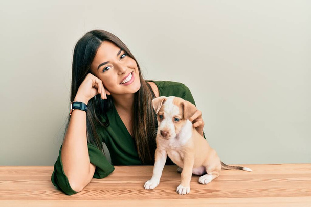 Young hispanic girl smiling happy and playing with dog sitting on the table over isolated white background. - 写真・画像