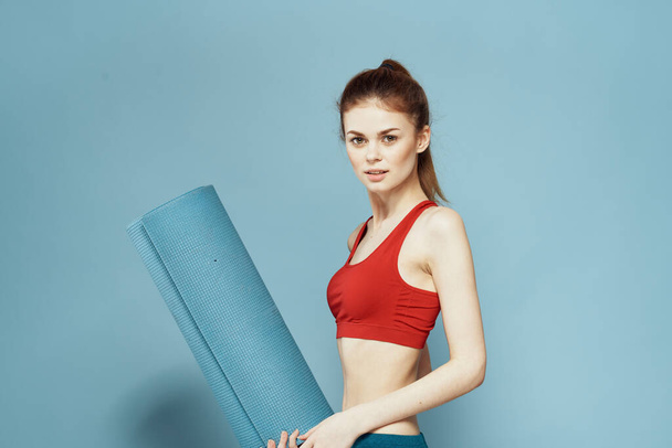 mujer atlética con el ejercicio de la estera de fitness figura delgada camiseta roja fondo azul - Foto, imagen