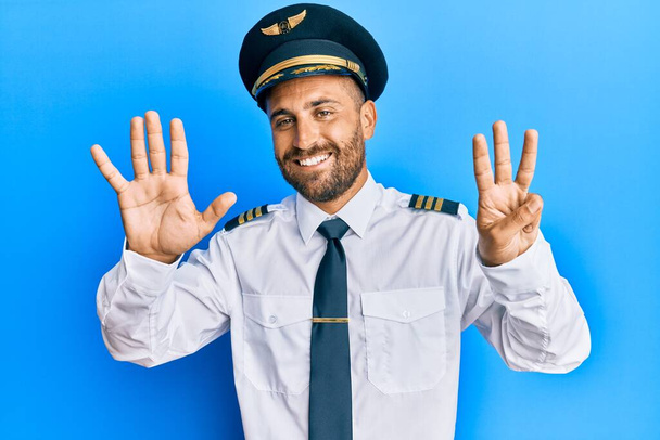 自信と幸せ笑顔ながら、飛行機のパイロットの制服を着て髭を生やしてハンサムな男は指の数8を示すと指摘します.  - 写真・画像