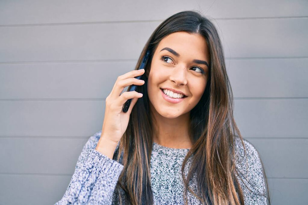 Mladý krásný hispánec dívka usměvavý šťastný mluvení na smartphone ve městě. - Fotografie, Obrázek
