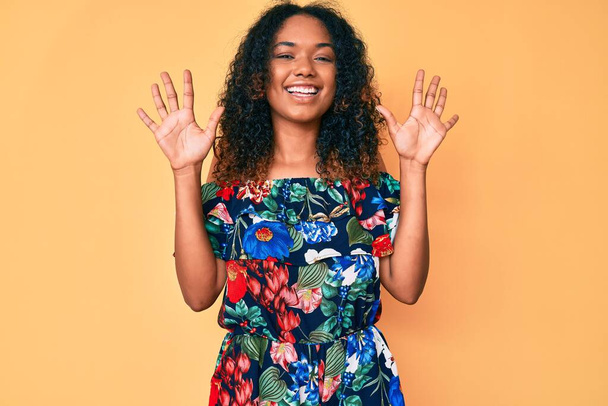Fiatal afro-amerikai nő alkalmi ruhát visel, mutatva és mutogatva a tízes számú ujjaival, miközben magabiztosan és boldogan mosolyog..  - Fotó, kép