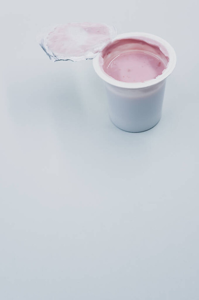 A vertical shot of an opened plastic container of fruit yogurt on a white surface - Foto, immagini