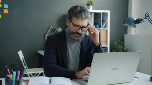 Exhausted mature man office worker typing with laptop then touching face feeling headache - Video