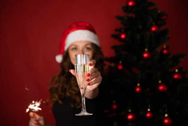 Feliz festa de Natal. Mulher em santa chapéu mantém copo de champanhe em foco - Foto, Imagem