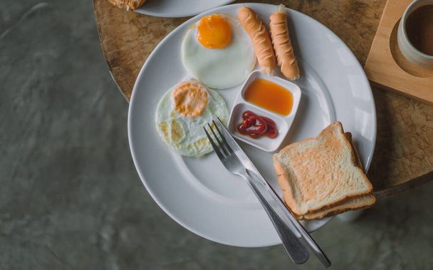 Kızarmış yumurtalı kahvaltı sosis ve beyaz tabakta ekmek ahşap bir masaya konur.. - Fotoğraf, Görsel