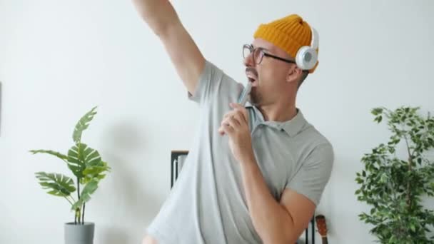 Young man dancing singing in remote control and listening to music through headphones indoors at home - Filmagem, Vídeo