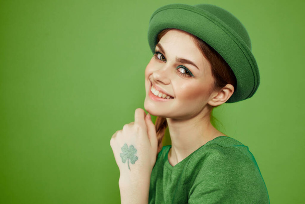 Leuk meisje met een shamrock op haar hand op een groene achtergrond vakantie St. Patricks Dag leuke hoed op haar hoofd  - Foto, afbeelding