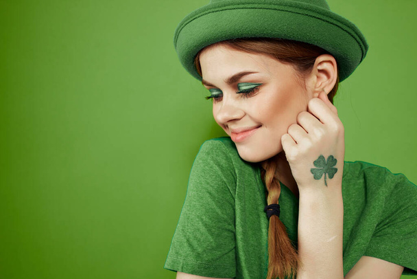 Buena chica con un trébol en la mano en un fondo verde vacaciones St. Patricks día divertido sombrero en su cabeza  - Foto, imagen