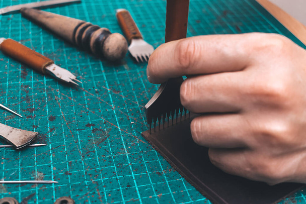 Men's hands make a leather product.Punching holes in the leather with a punch.Tools for leather craft.Top view - 写真・画像