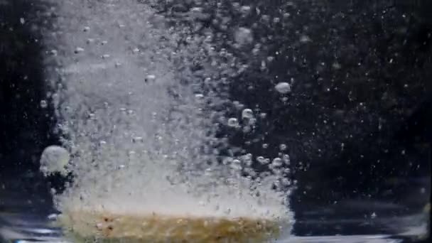 Macro shot de tableta efervescente se disuelve con burbujas en agua, cámara lenta - Metraje, vídeo