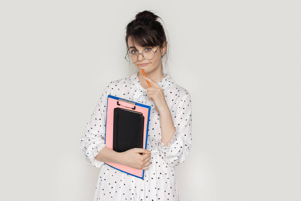 Brunette woman with glasses is holding some folders and posing on a white studio wall - Foto, Imagen