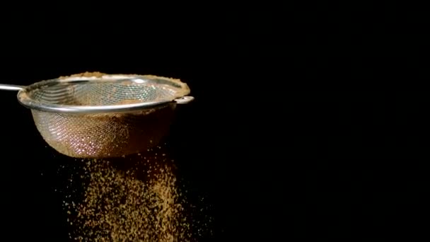 Ανοικτή καφέ σκόνη κοσκινίσματος με κόσκινο, αργή κίνηση απομονωμένη σε μαύρο φόντο - Πλάνα, βίντεο