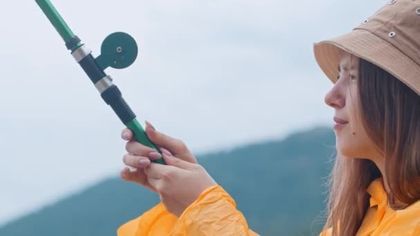 Γυναίκα στρίβοντας το πηνίο μιας ράβδου αλιείας και κοιτάζοντας το άγκιστρο - Πλάνα, βίντεο