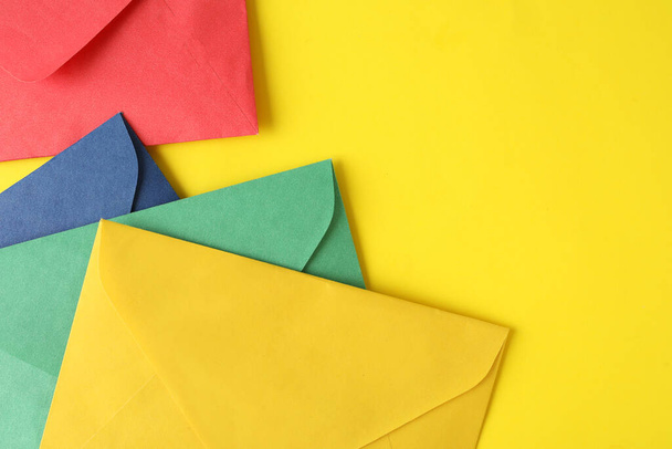 Colorful paper envelopes on yellow background, top view. Space for text - Zdjęcie, obraz