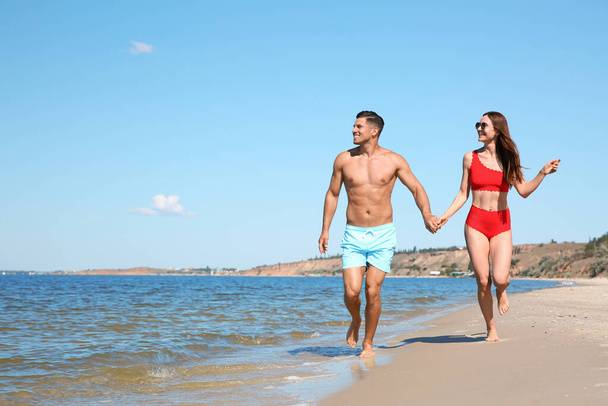 Woman in bikini and her boyfriend on beach, space for text. Happy couple - Zdjęcie, obraz