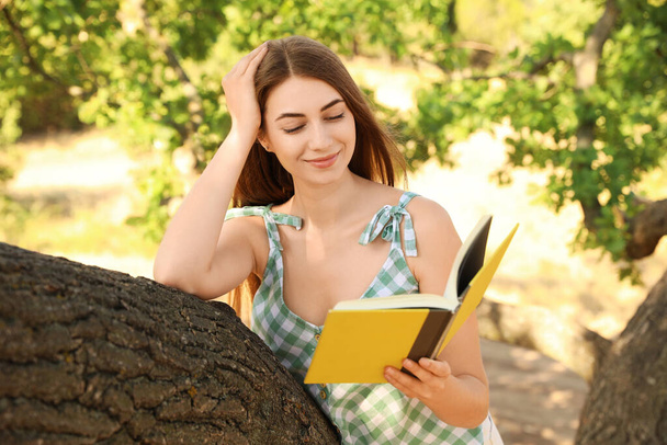 Young woman reading book on tree in park - Valokuva, kuva