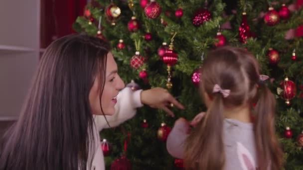 Genç, güzel bir anne ve Noel ağacını süsleyen tatlı küçük bir kız. - Video, Çekim