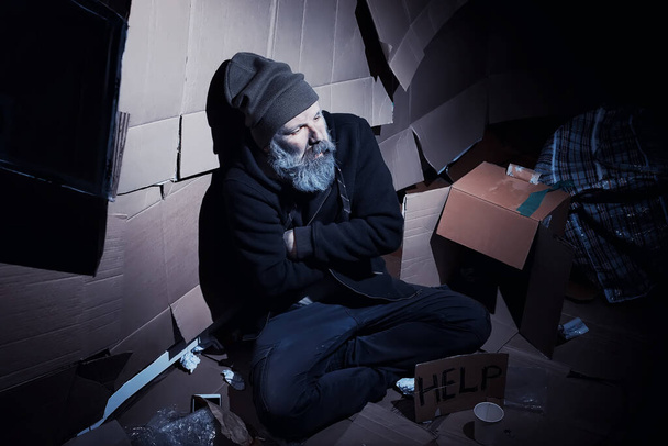 Бездомний бородатий чоловік сидить на коробках на вулиці і просить про допомогу. Потрібна безпритульна людина просить гроші на їжу і на ніч
. - Фото, зображення