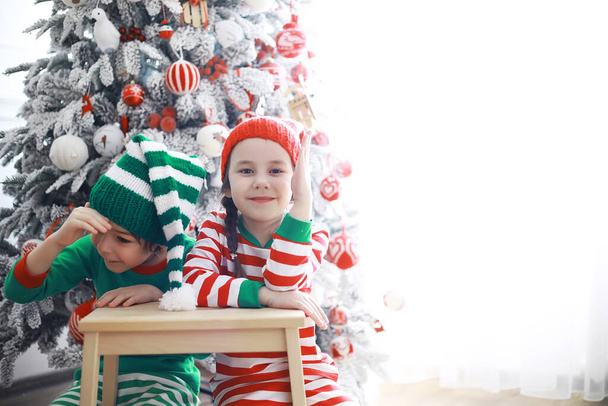 Los niños lindos en trajes de elfo de Navidad en una habitación bellamente decorada para la Navidad. Tiempo de milagros. Regalos de Santa Claus - Foto, imagen