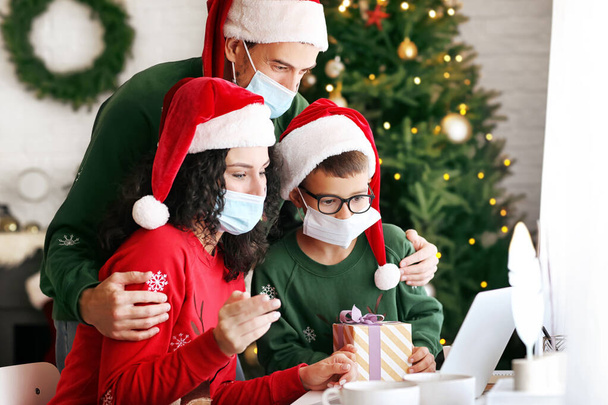 家庭でクリスマスを祝うラップトップを持つ家族コロナウイルスの流行のために - 写真・画像
