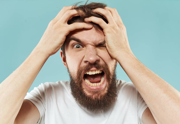 Modèle homme barbu en T-shirt blanc sur fond bleu irritabilité émotions modèle - Photo, image