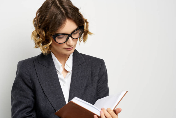 Klasik takım elbiseli bir iş kadını elinde bir not defteri ve yüzünde gözlüklerle. - Fotoğraf, Görsel