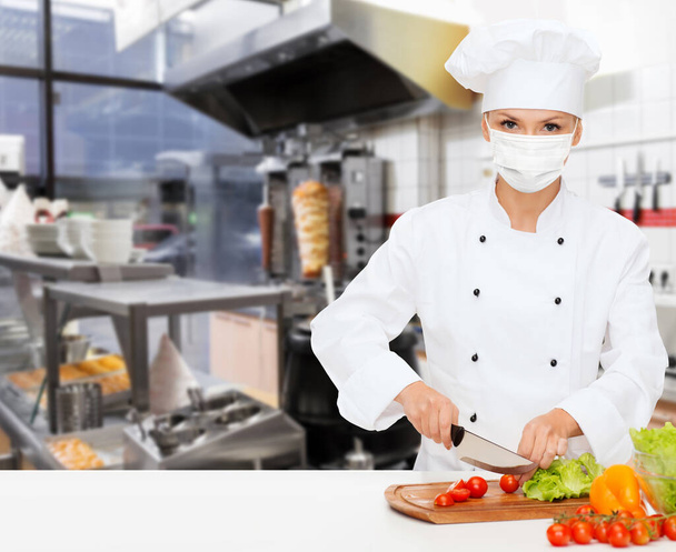 female chef in mask cutting vegetables at kitchen - Фото, зображення