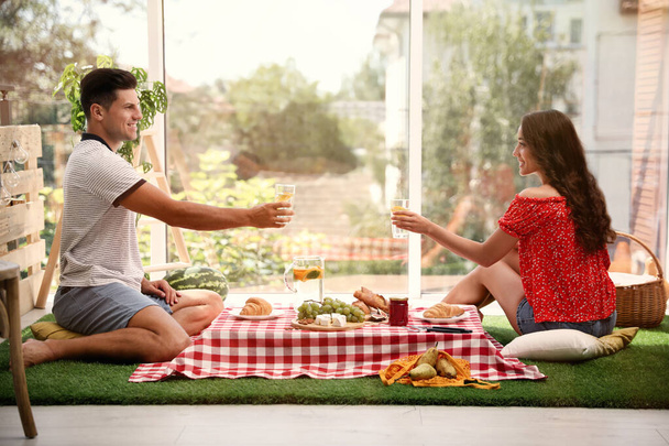 Gelukkig paar met verfrissende drankjes imiteren picknick thuis - Foto, afbeelding