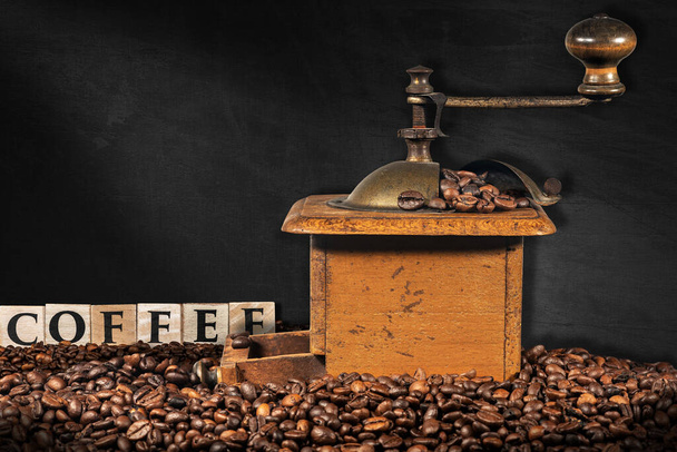 Oude handmatige koffiemolen met gebrande koffiebonen en de tekst Koffie gemaakt van houten blokken, op een leeg schoolbord met kopieerruimte. - Foto, afbeelding