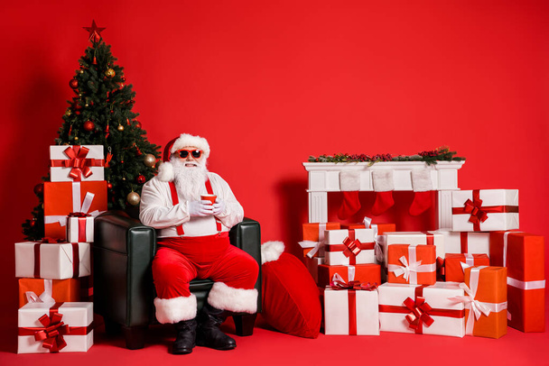 Portrait of his he nice attractive funky fat overweight cheerful Santa sitting in armchair drinking beverage in decorated room isolated bright vivid shine vibrant red color background - Valokuva, kuva