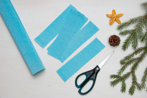 紙からクリスマスツリーを作る。薄いテーブルの上にはさみ、青い紙、およびモミの枝。オリジナルの子供向けアートプロジェクト。DIYのコンセプト。ステップバイステップの写真の指示。ステップ2. - 写真・画像