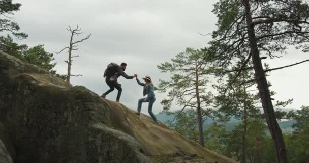 Чоловік допомагає жінці піднятися на скелю. Він тягне її за руку. Вони дивляться на природу. Поїздка в гори. 4K DCI - Кадри, відео