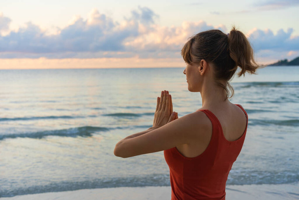 Attractive young woman wearing sportswear practicing yoga alone. Yogi female stretching and exercising outdoors by the sea. Copy space, background. Achieving zen concept. - Photo, Image