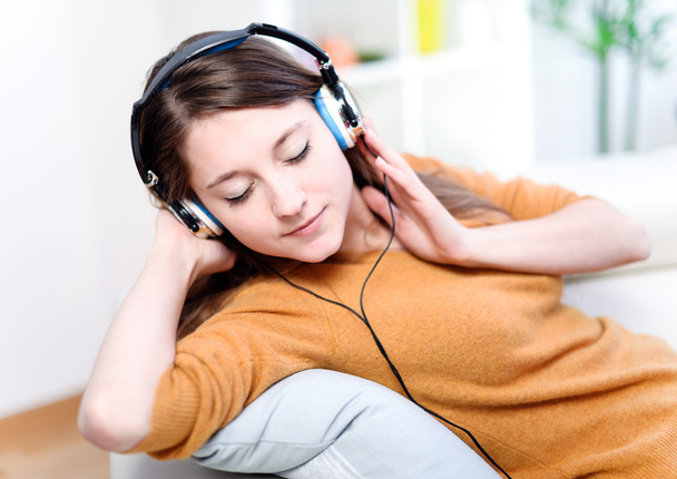 Beautiful relaxed young woman listening of the music by being lengthened on her sofa - Fotoğraf, Görsel