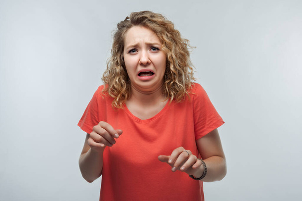 Image of dissatisfied blonde girl with curly hair in casual t shirt doing disgust face because aversion reaction with hands raised. Studio shot, white background. Facial expression concept - Foto, Imagen