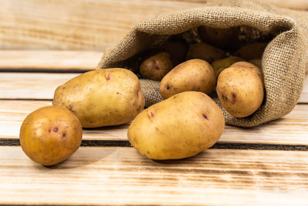 Batatas frescas em um saco velho em um fundo de madeira. Espaço livre para texto. - Foto, Imagem