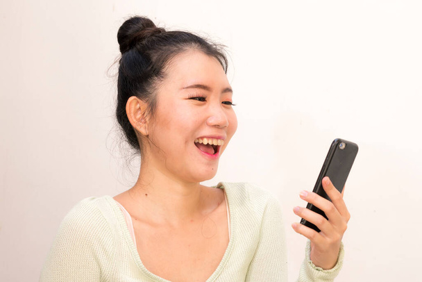 natural portrait of young attractive and sweet Asian Chinese woman laughing happy and cheerful using internet mobile phone isolated on studio background in communication concep - Foto, Imagem