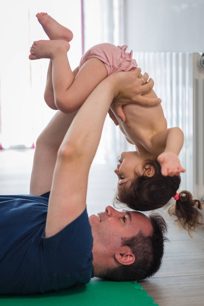 Père caucasien fait du sport, fitness et yoga avec sa petite fille de mère latine dans la salle à manger de la maison, ils s'amusent pendant qu'ils font les exercices. - Photo, image
