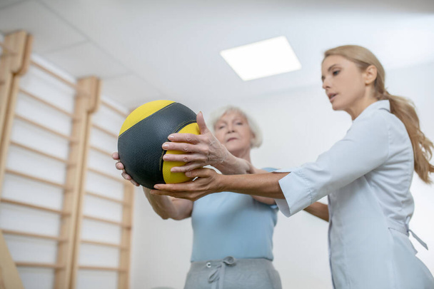 Idős nő gyakorol labdával egy rehabilitációs központban - Fotó, kép