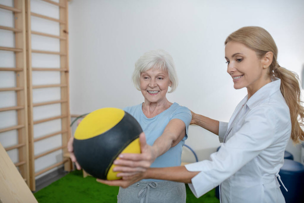 Grey-haired woman exercising with a ball in a rehabilitation center - 写真・画像