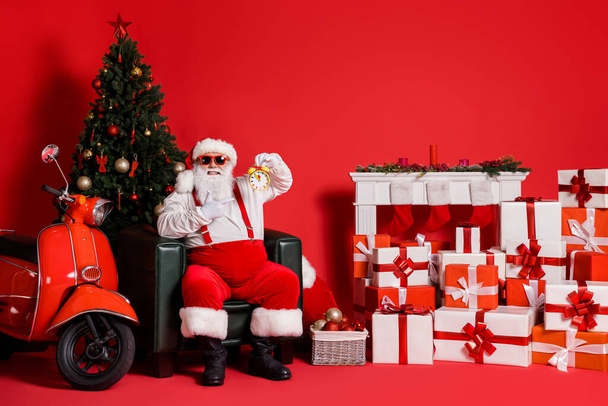 Nice attractive fat overweight cheerful Santa sitting in armchair showing time management fast delivery midnight holly jolly isolated over bright vivid shine vibrant red color background - Foto, Bild