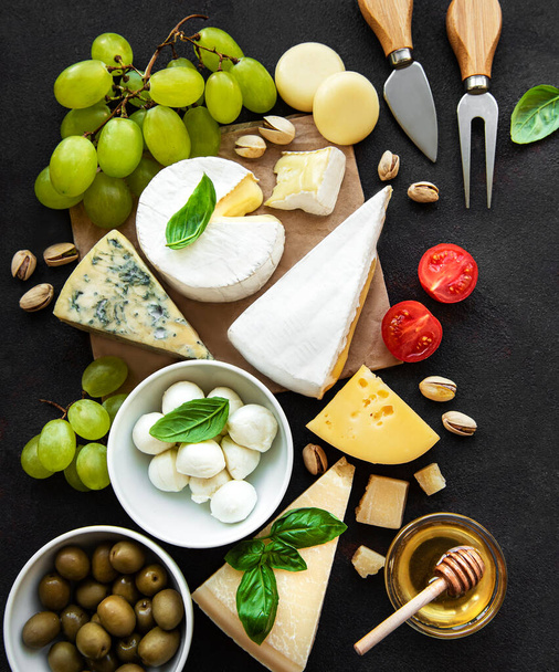 Varios tipos de queso, uvas, miel y aperitivos sobre un fondo de hormigón negro - Foto, imagen
