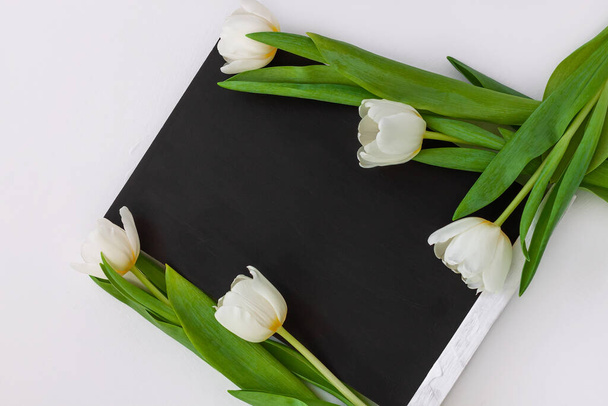 Black chalk board mockup with tulip flowers on white background. Blackboard menu with easel, spring sales. Copy space frame ad text content. Blank inscription template. Education advertisement display - Foto, Bild