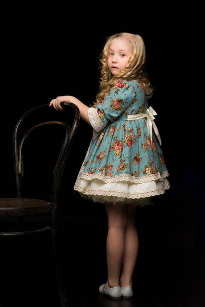 Portrait of a girl standing on a black background near the old Viennese chair. - Fotoğraf, Görsel