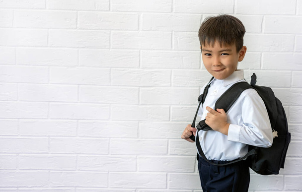 little boy with backpack shows tongue against white brick wall background back to school copy spase - Foto, afbeelding