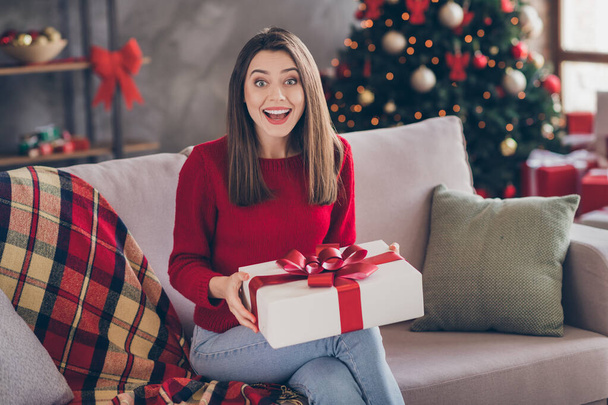 Photo of shocked girl sit couch hold x-mas receive gift box in house indoors with christmas tinsels decoration - Foto, immagini