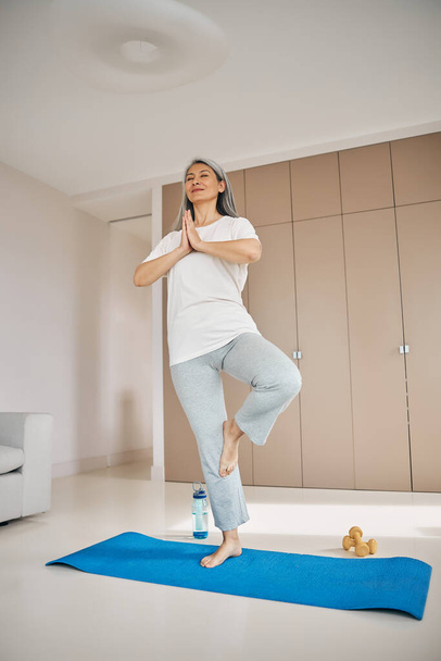 Thoughtful woman in sportswear standing on yoga mat in room indoors - Foto, Imagem