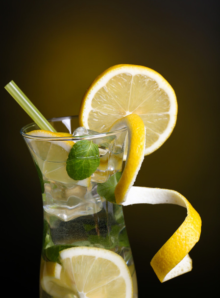 Glass of cocktail with lemon and mint on dark yellow background - Photo, Image