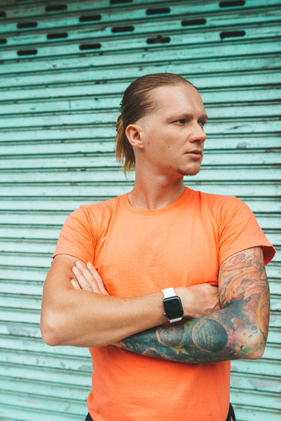 Portrait of a man in orange t-shirt at the metal blue garage door - Fotografie, Obrázek